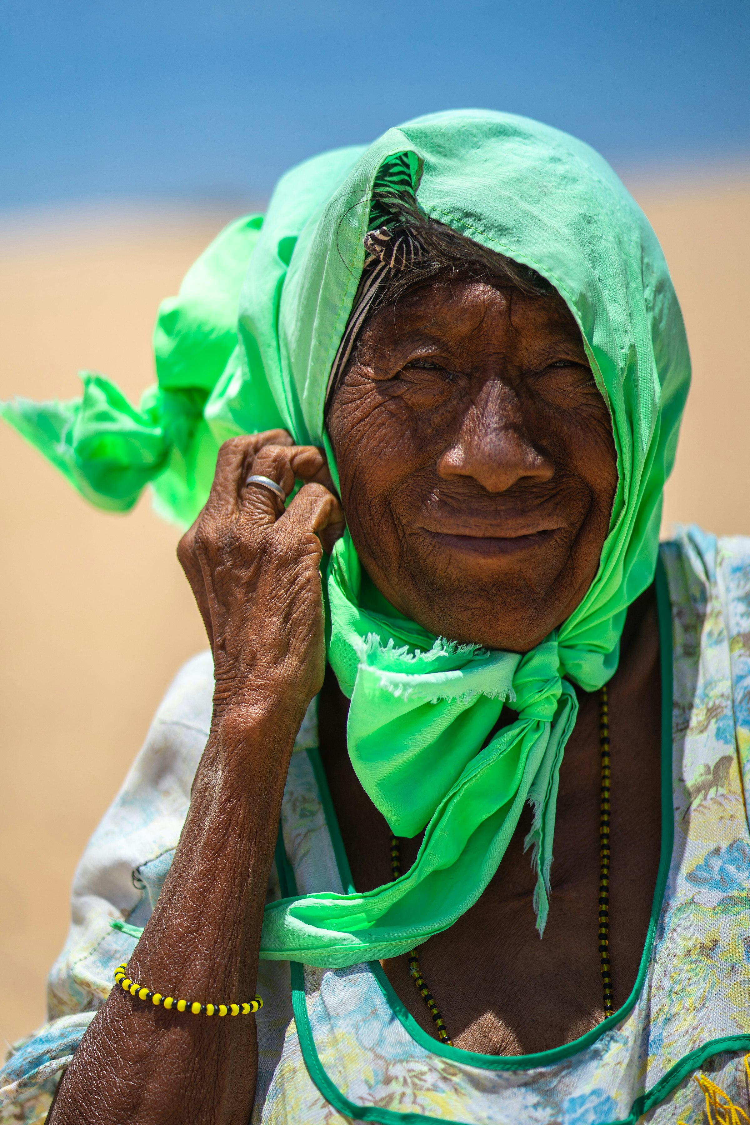 Close portrait of an elderly Wayuu woman in a green headscarf in the La Guajira desert, Colombia, looking at the camera with a dignified expression
