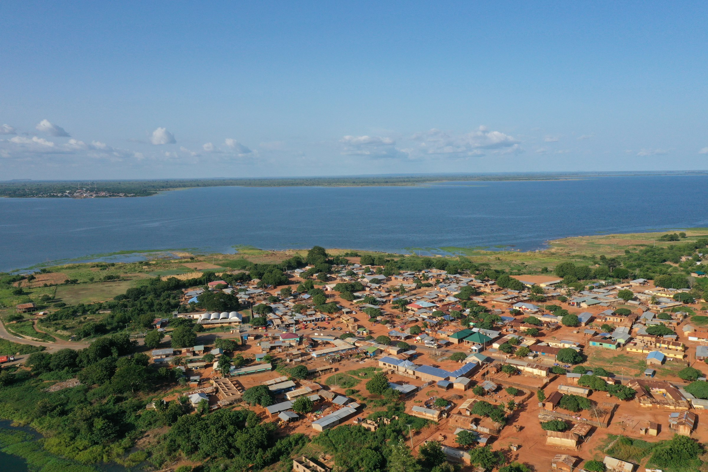 Aerial view of a lakeside village on the shore of a large lake in Ghana, with red-earth roads and scattered rooftops