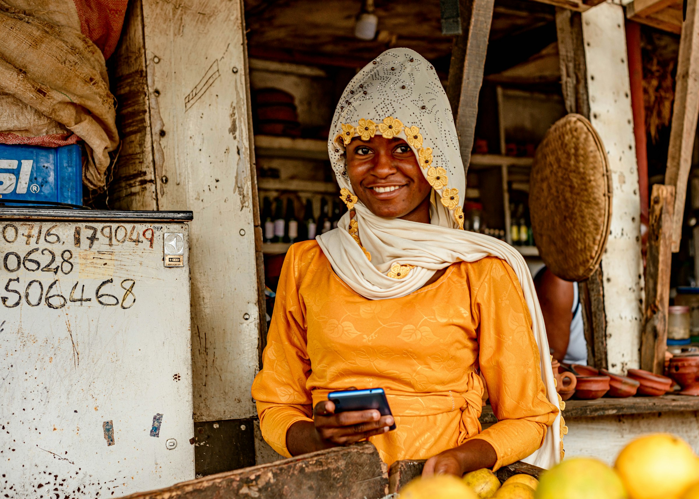 Woman at a fruit stall in Dar es Salaam, Tanzania holding a smartphone