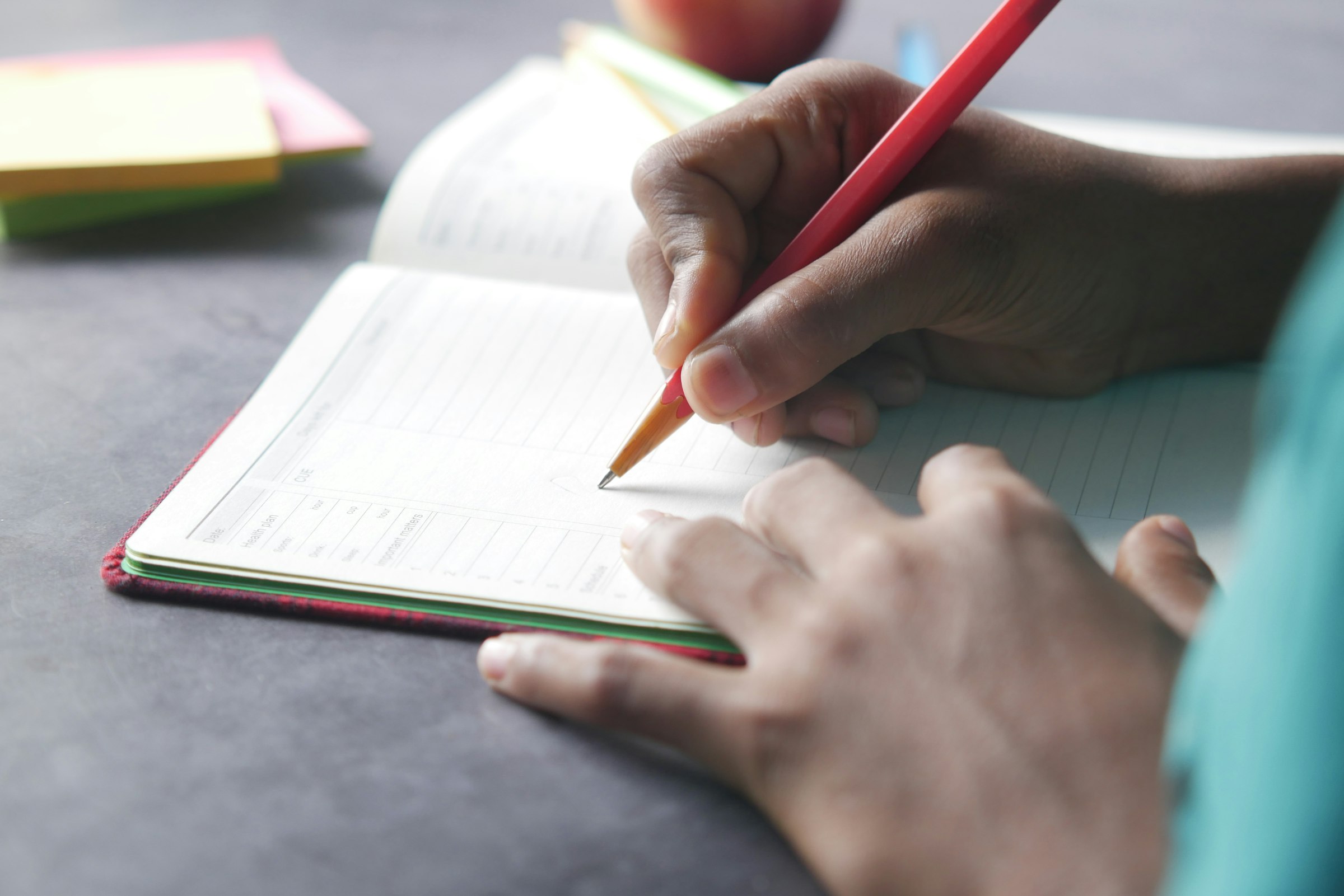 Close-up of a hand writing in a notebook with a pencil
