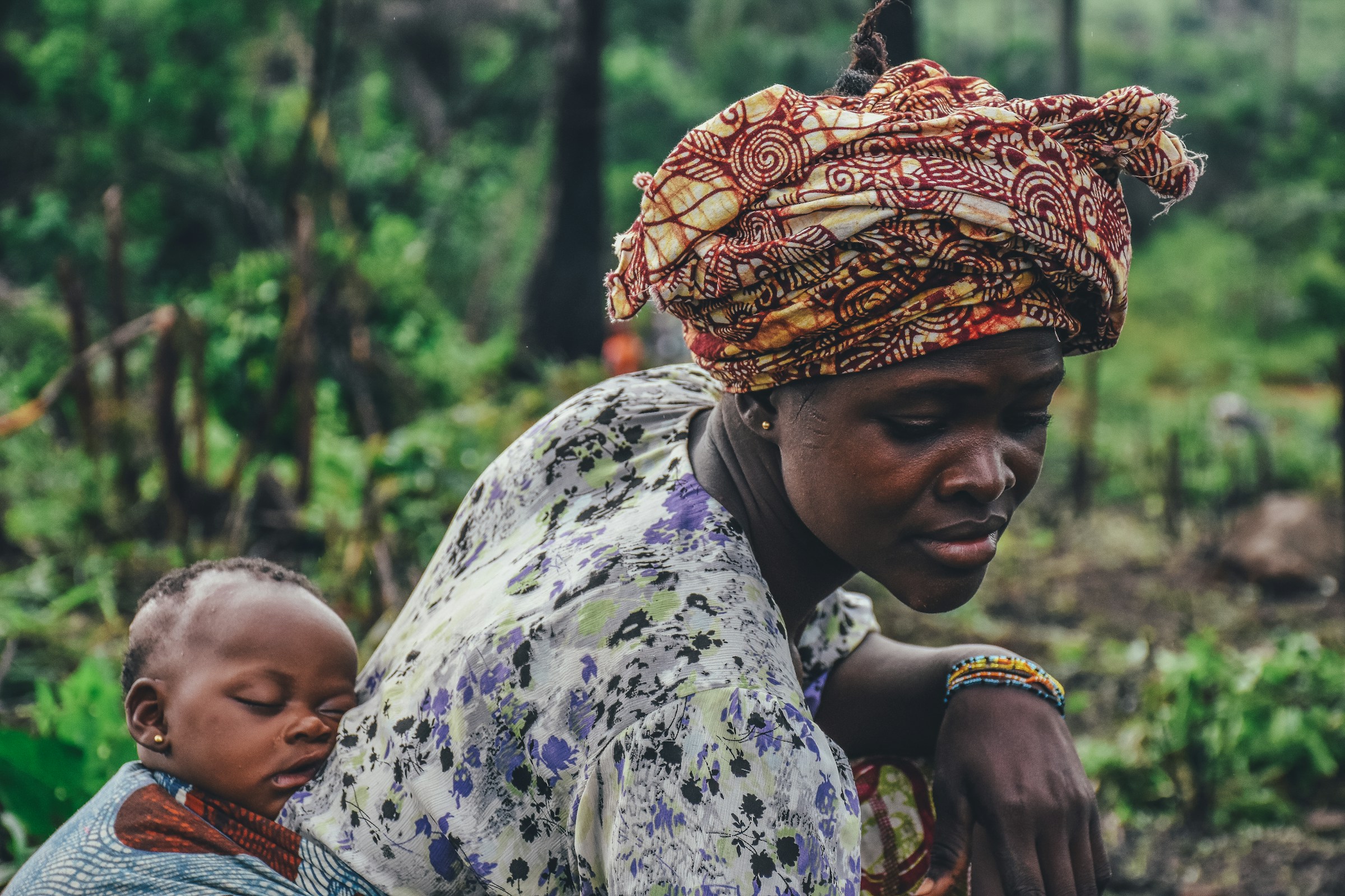A mother carrying her sleeping infant in a traditional sling while working