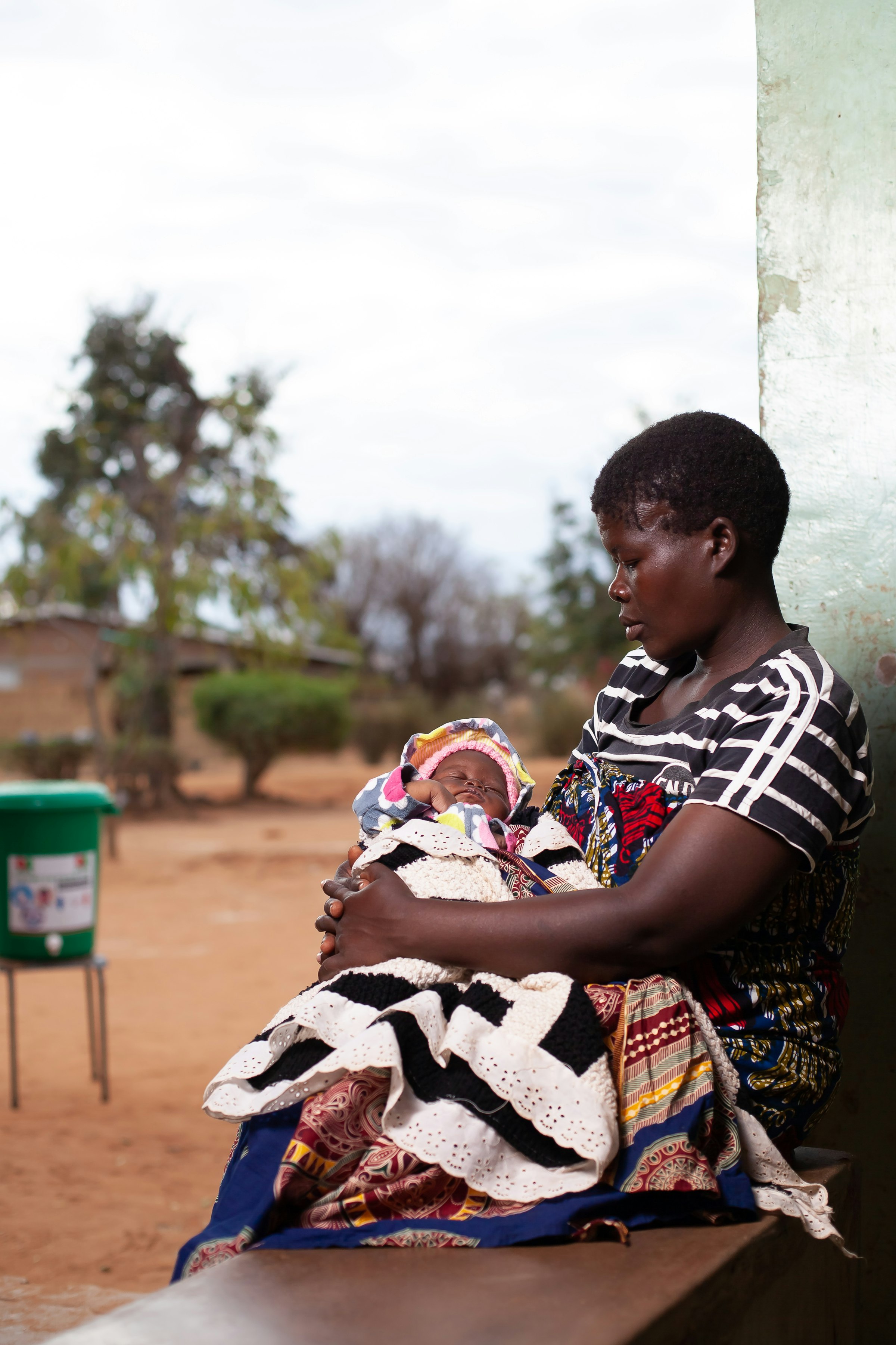 Mother holding her newborn baby outside a rural health post in Ntcheu District, Malawi
